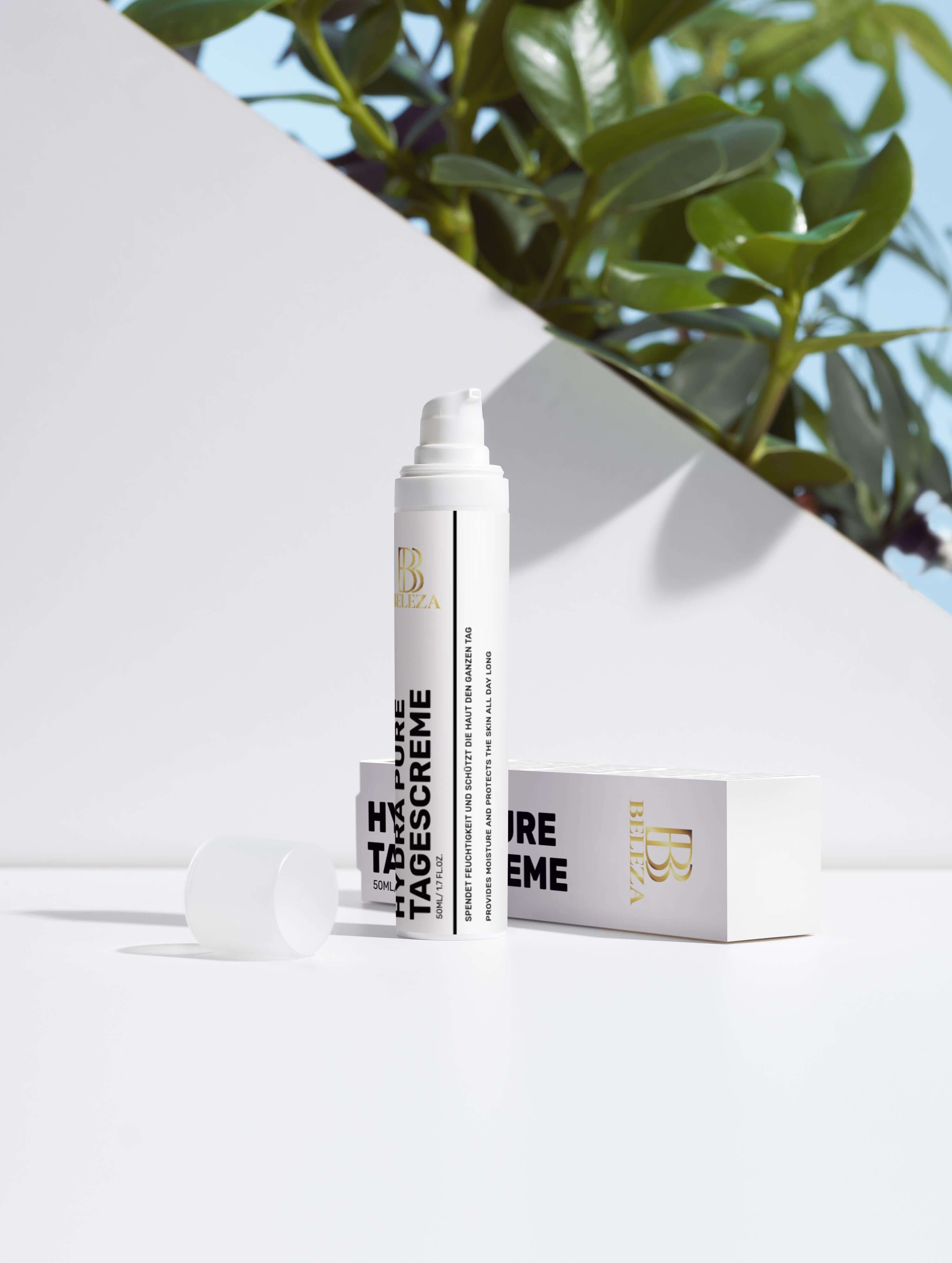 Hydra Pure Tagescreme packaging on a bright surface with greenery in the background, promoting radiant skin.